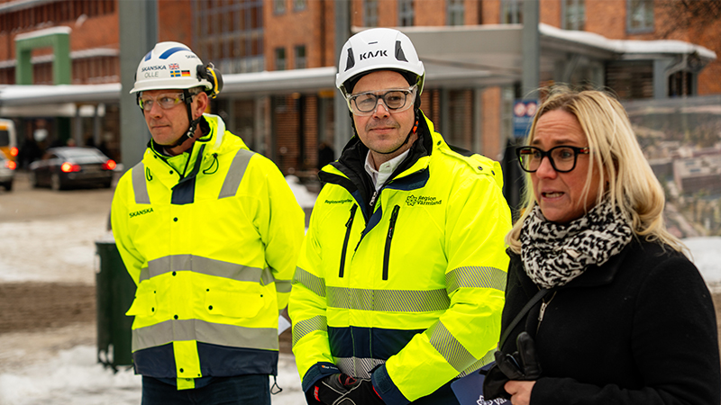 Tre personer utomhus, två med reflexvästar och hjälmar.