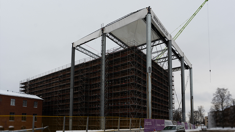 Foto på byggnad med byggnadsstomme runt och tältskydd över taket.