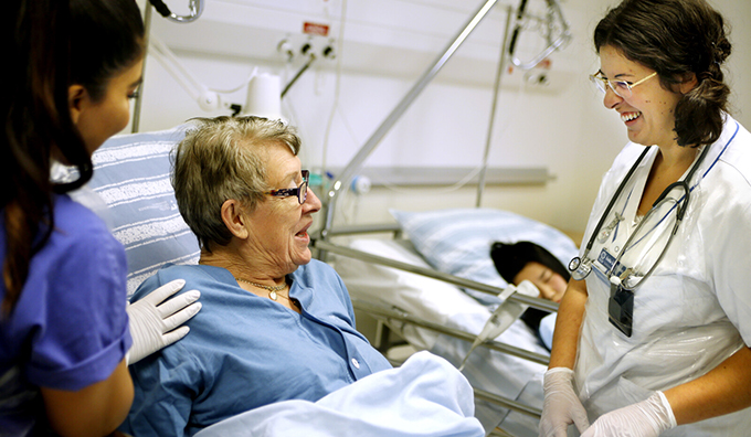 Patient i säng med två sjuksköterskor bredvid.