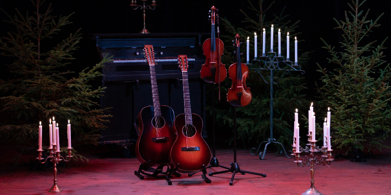 En scen med fioler, gitarrer, granar och levande ljus.