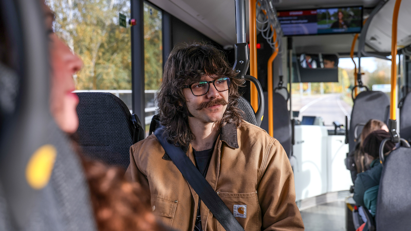 En kille som sitter ombord en buss och ser glad ut. 