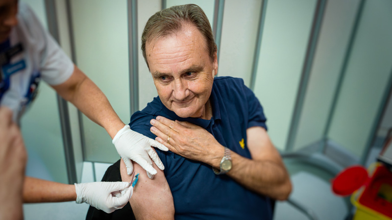 En person blir vaccinerad. Han har kavlat upp tröjärmen samtidigt som en sjuksköterska sätter sprutan i hans överarm.