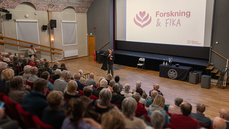 En fullsatt samlingssal med åskådare som syns bakifrån. Längst fram på scenen står en föreläsare.