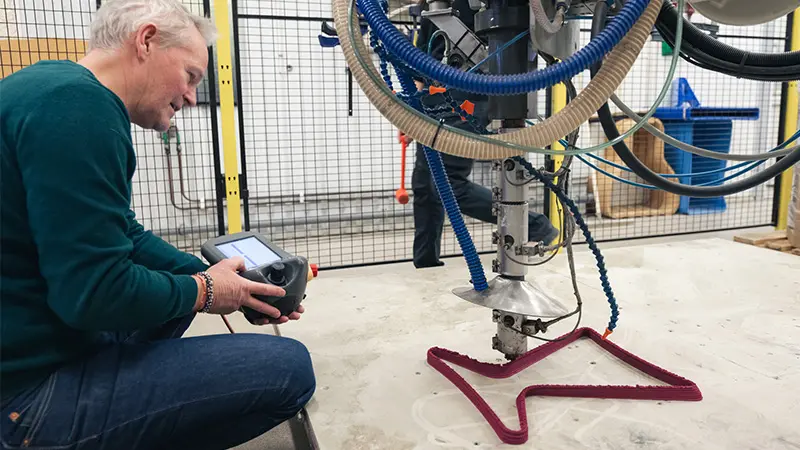 A man operates a machine that shapes a horizontal pink figure.