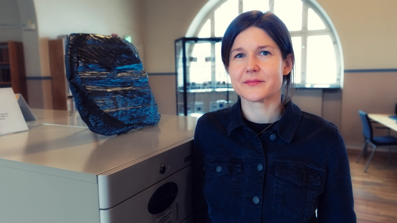 En person står framför en svart träskulptur. I bakgrunden syns ett stort ovalt fönster.