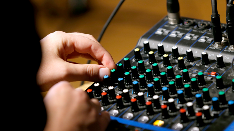 Händer skruvar på knappar på ett mixerbord. 