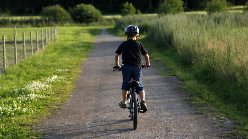 En pojke som cyklar på en grusväg med gröna fält på vardera sida.
