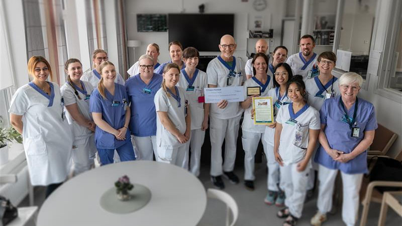 En grupp medarbetare i hälso- och sjukvårdens vita kläder visar upp ett diplom.