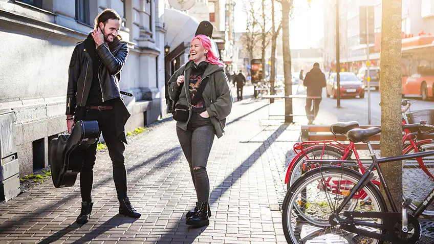 Två personer med gitarrfodral går på en trottoar. 