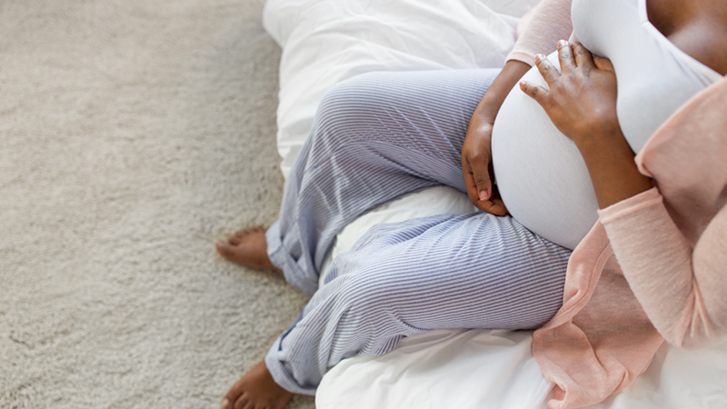 gravid kvinna sitter i en säng och håller händerna på magen