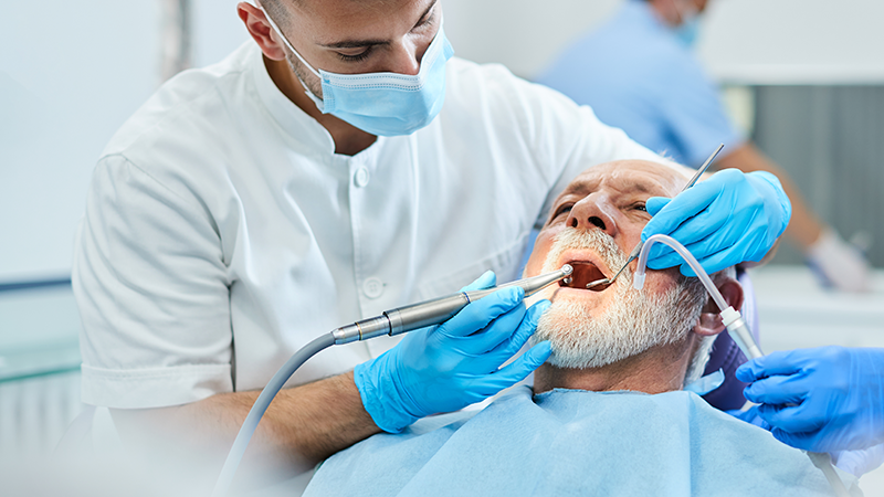 en äldre man blir undersökt i munnen i en behandlingsstol