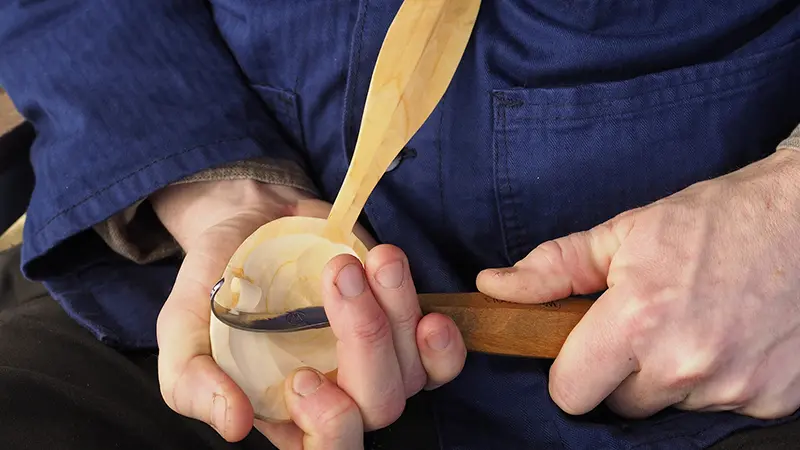 Närbild på händer som täljer en träsked.