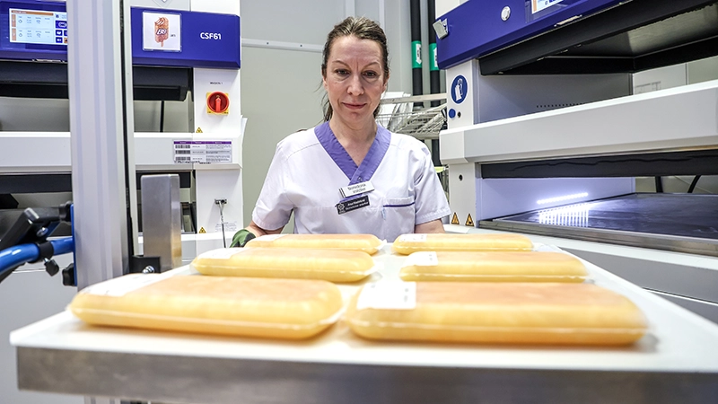 En sköterska står framför en bricka med flera påsa plasma. 