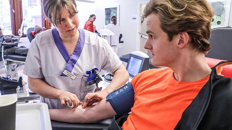 Närbild på sköterska som sätter en nål i armen på en plasmagivare. 