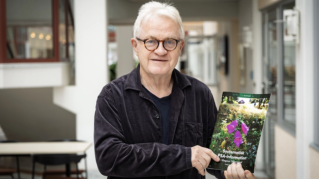 En person håller upp en tryckt rapport. På framsidan syns en lila blomma.