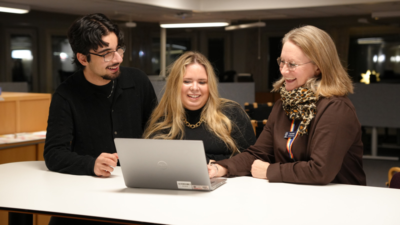 Två ungdomar och en vuxen person pratar med varandra vid en dator.