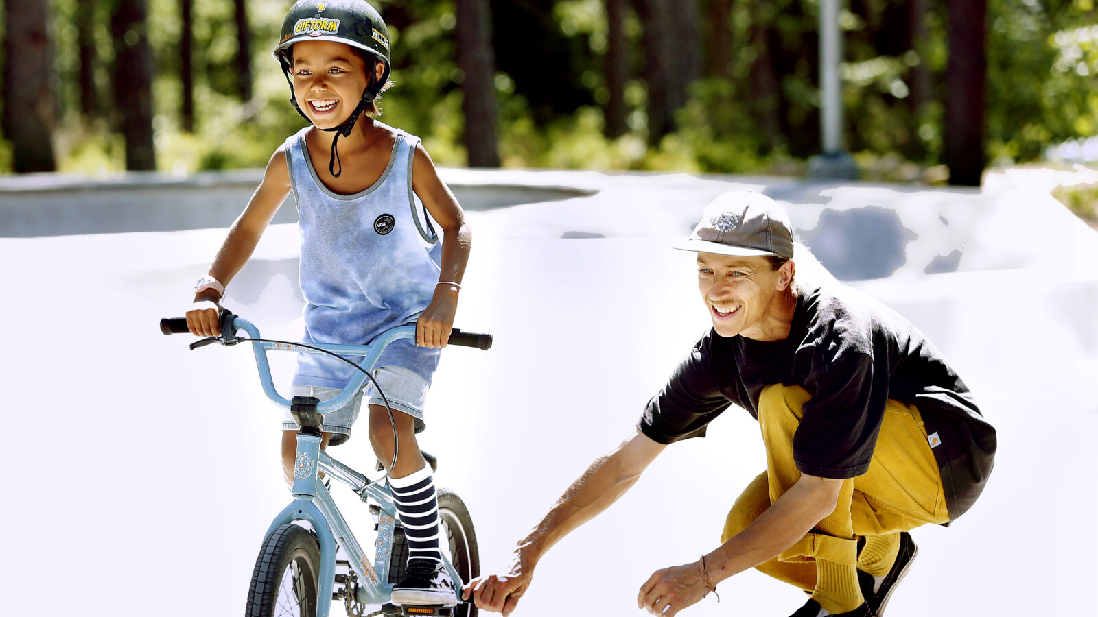 Barn som cyklar och drar sin pappa på skateboard efter. 