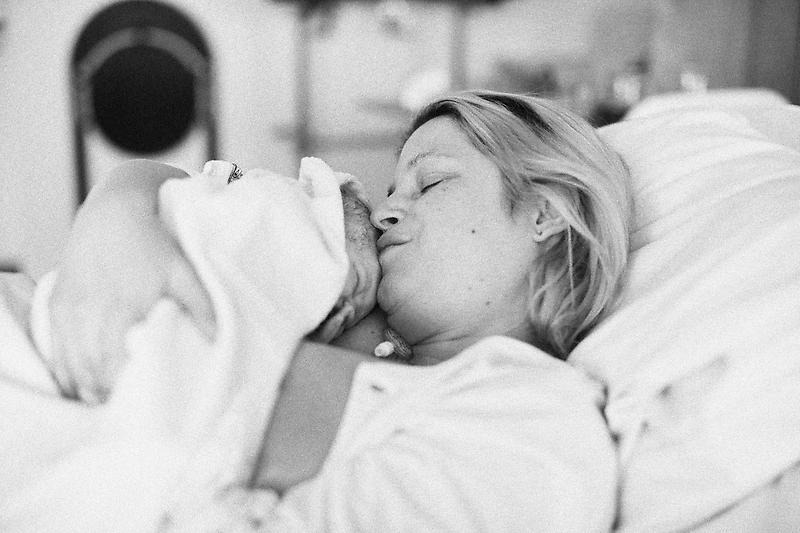 En kvinna i en säng med nyfödd bebis i famnen. 