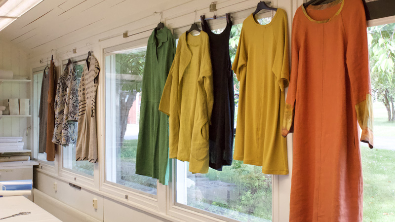 Färgglada plagg i linne hänger i fönstret i en syateljé. 