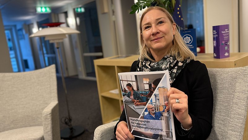 Glad kvinna som sitter i ett kontorslandskap och håller i en rapport.