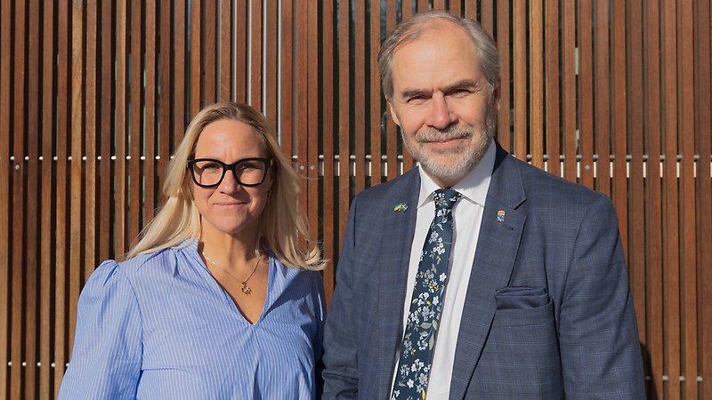 En kvinna och man står utomhus vid en vägg och ser glada ut.