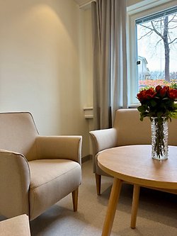 Väntrummet vid bårhuset i Kristinehamn. Det är möblerat med ljusa fåtöljer och ett träfärgat bord med en vas med orange rosor i. 