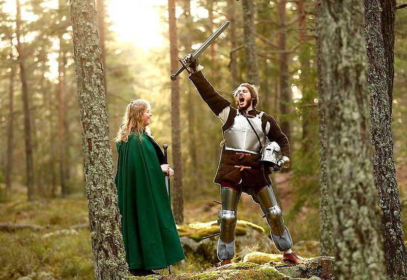 Två personer i skogen som är utklädda med mantlar och svärd