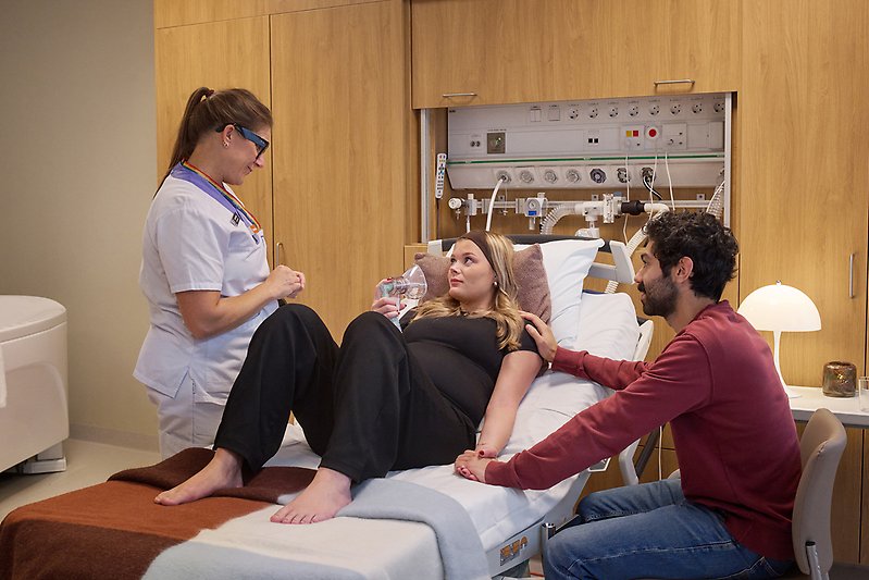 Gravid kvinna håller i mask, vårpersonal och man bredvid.
